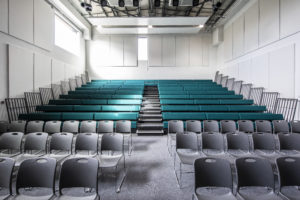 Photo of the inside of the main conference hall in the Leigh Academy Blackheath building, showing tiered seating facing towards the front of the room.