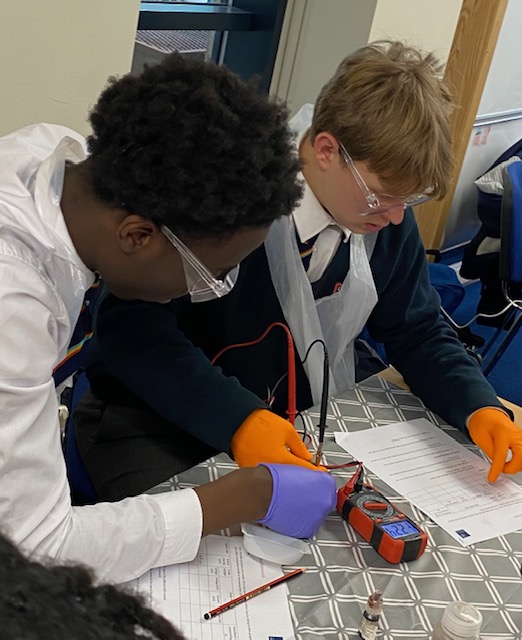Two male students are seen wearing lab coats and goggles and conducting a Science experiment at Oxford University.