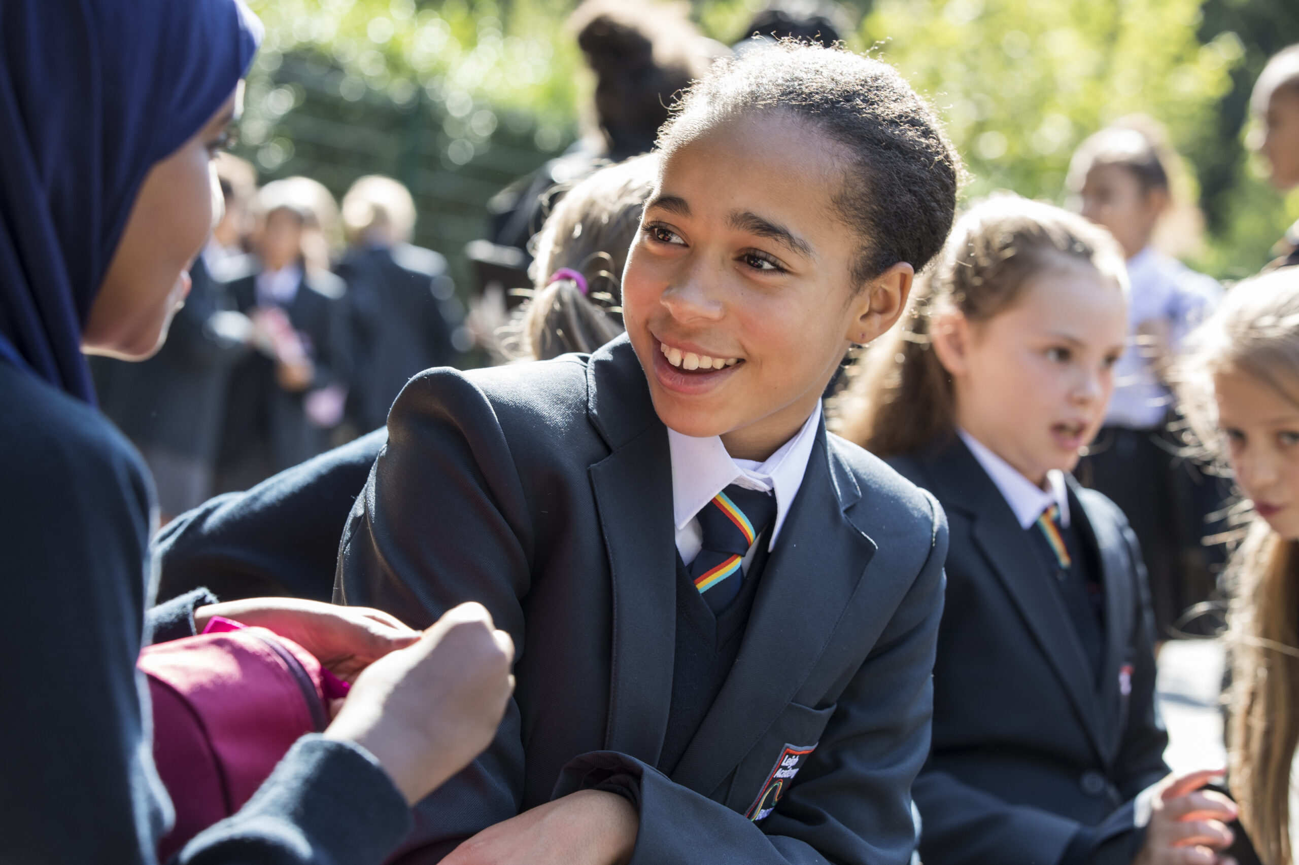 A female student is seen outdoors with a large group of others, wearing academy uniform and smiling at another student.