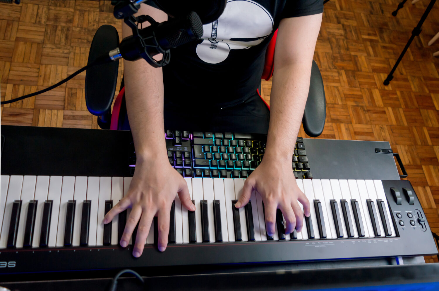 top view of unrecognizable man sitting playing the electric piano at home with a condenser microphone near his face.