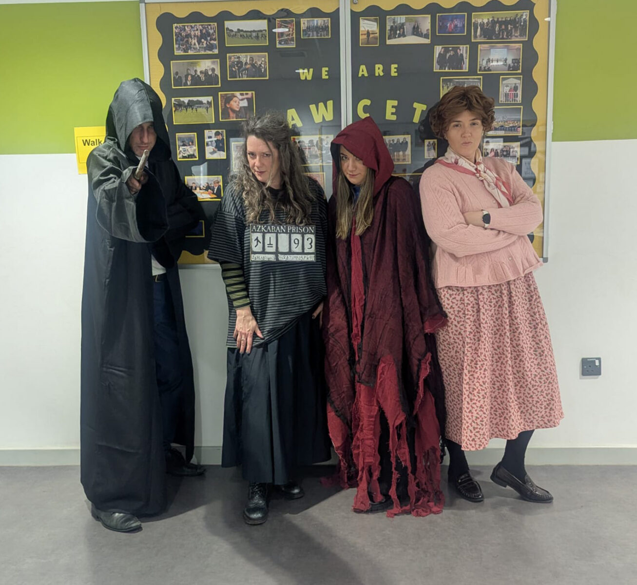 Four adults posing in a hallway dressed in Harry Potter-themed costumes, including a cloaked figure, an Azkaban prisoner, a person in tattered robes, and a character in a pink cardigan.