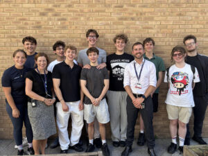Mixture of students and teacher standing outside smiling against a brick wall